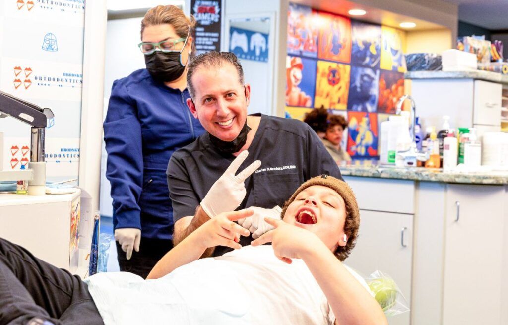 Dentist smiling beside reclining patient in a clinic, with staff in the background