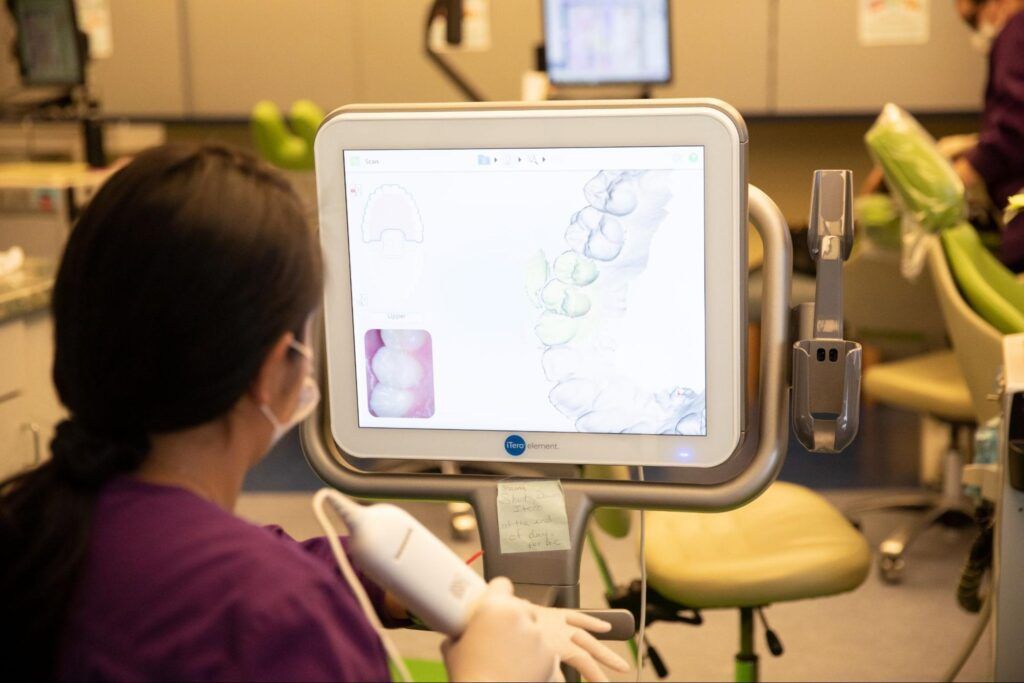 Person viewing a medical scan on a monitor in a dental clinic, with a handheld scanner in the foreground