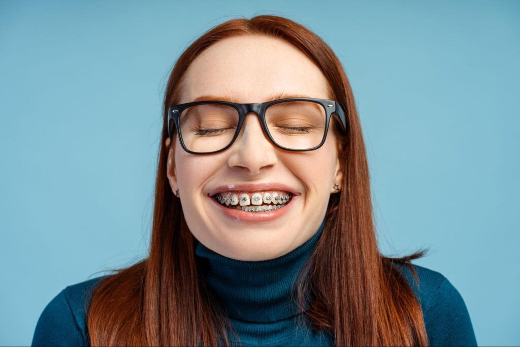 Smiling person with glasses and braces against a blue background