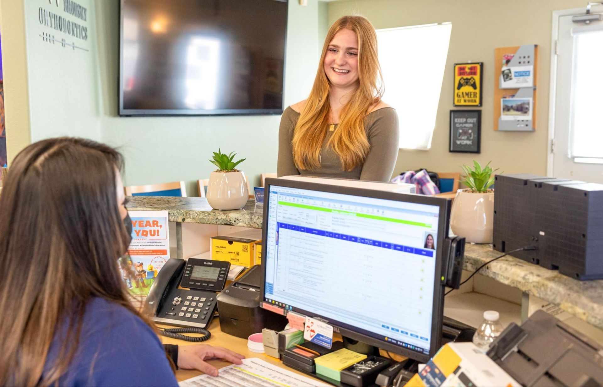 Reception desk with two women, one seated at a computer and one standing and smiling behind the counter