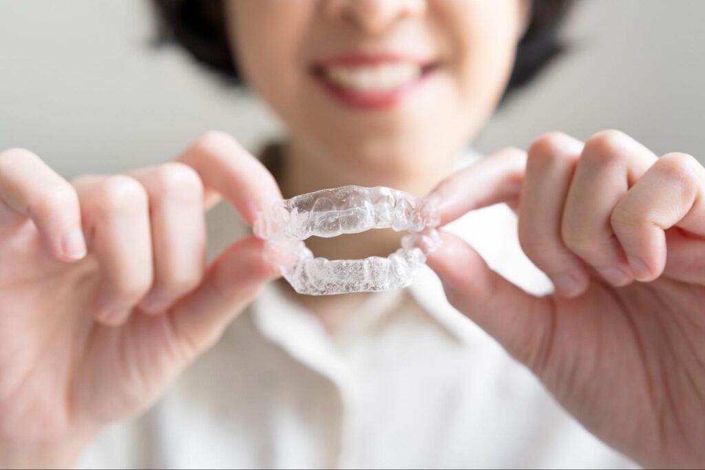 Hands holding a clear orthodontic aligner in front of a smiling person