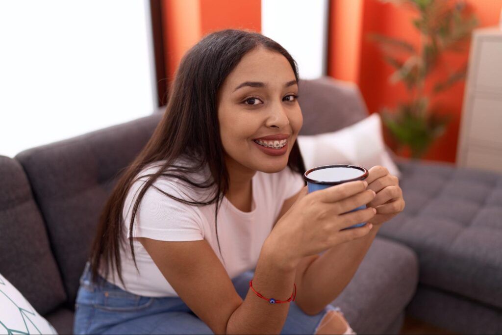 Smiling woman sitting on a couch, holding a mug in a cozy living room.