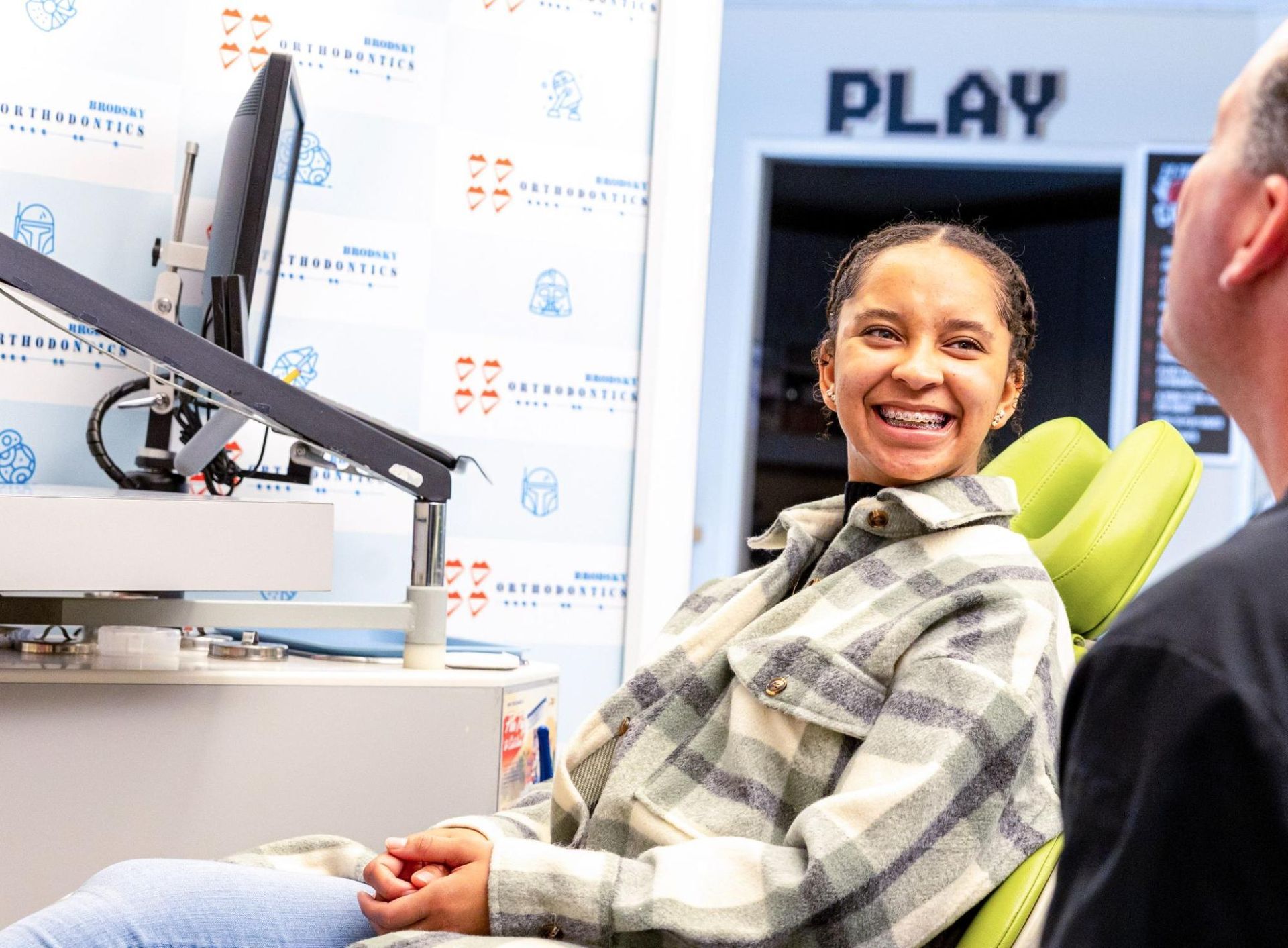 Person smiling in a clinic chair using a screen-mounted device labeled “PLAY”