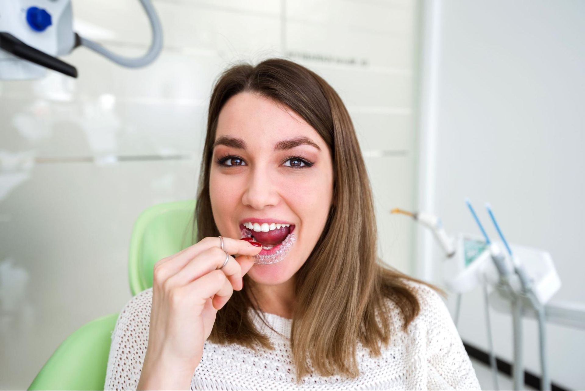 Woman flossing teeth in a dental clinic, smiling while seated in a dentist’s chair.
