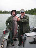 Two people in rain gear holding a large fish on a boat on a lake