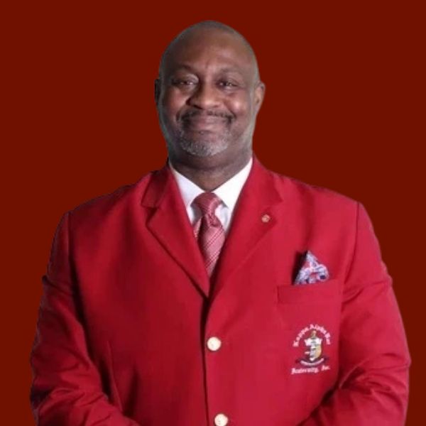 Man in red suit and bow tie, looking directly at the viewer against a red background.