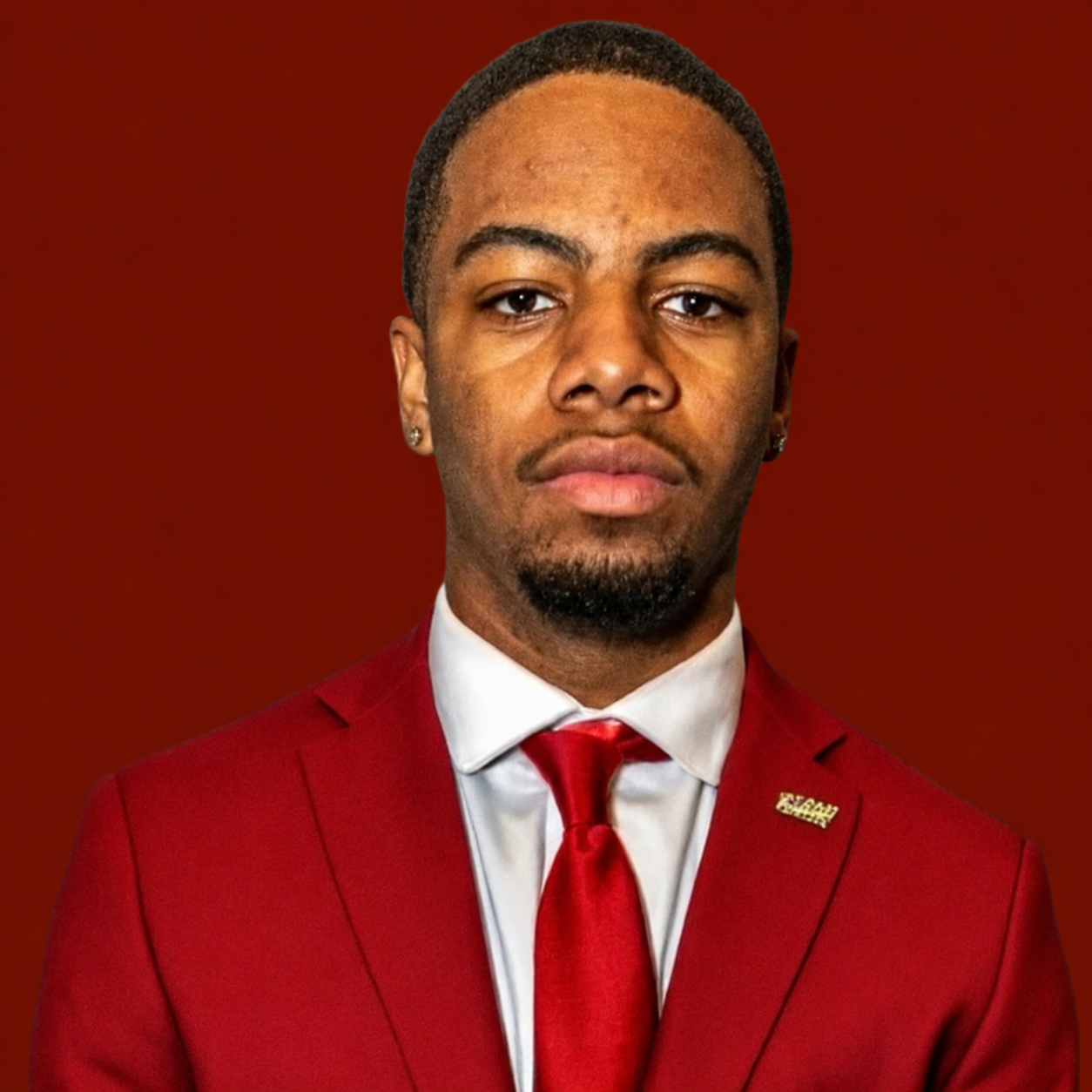 Man in maroon suit, red tie, and white shirt, against a maroon background.