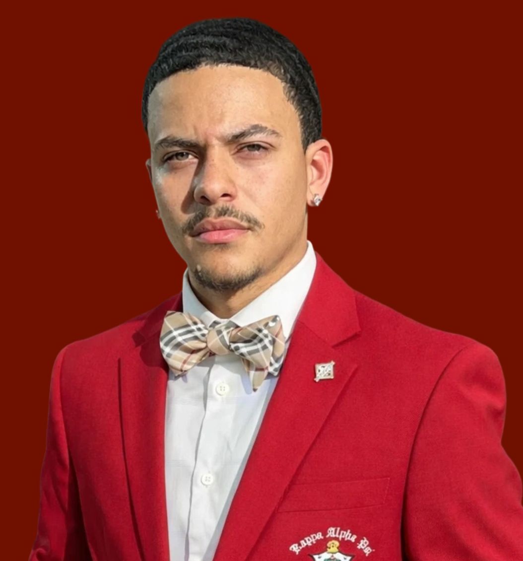 Man in a red suit and tie, smiling broadly against a red background.