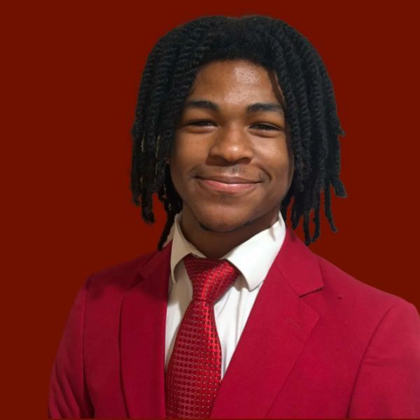 Young Black man in maroon suit and tie, serious expression.