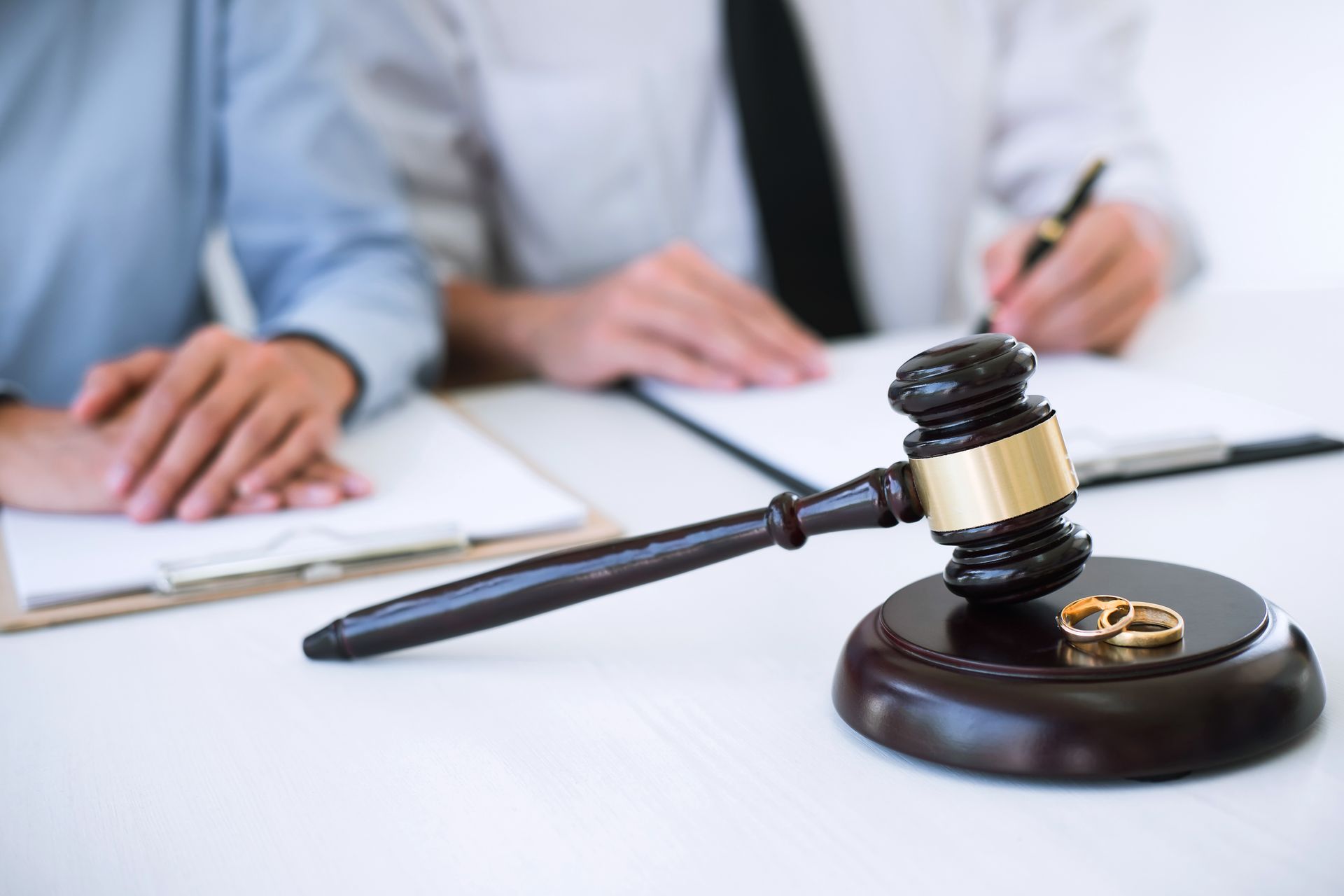 Gavel and wedding rings on a stand, people in business attire, one writing on a document.