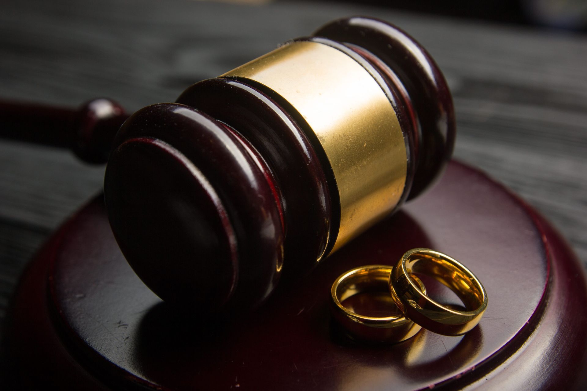 Judge’s gavel beside two gold wedding rings on a dark wooden surface