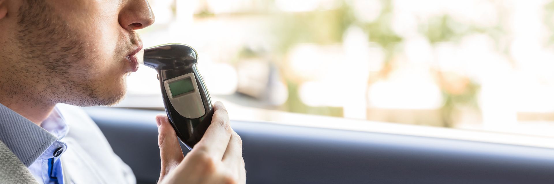 Person speaking into a handheld microphone inside a car, looking out the window.