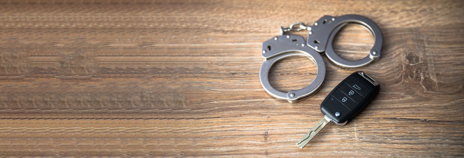 Metal handcuffs and a black car key on a wooden surface, viewed from above