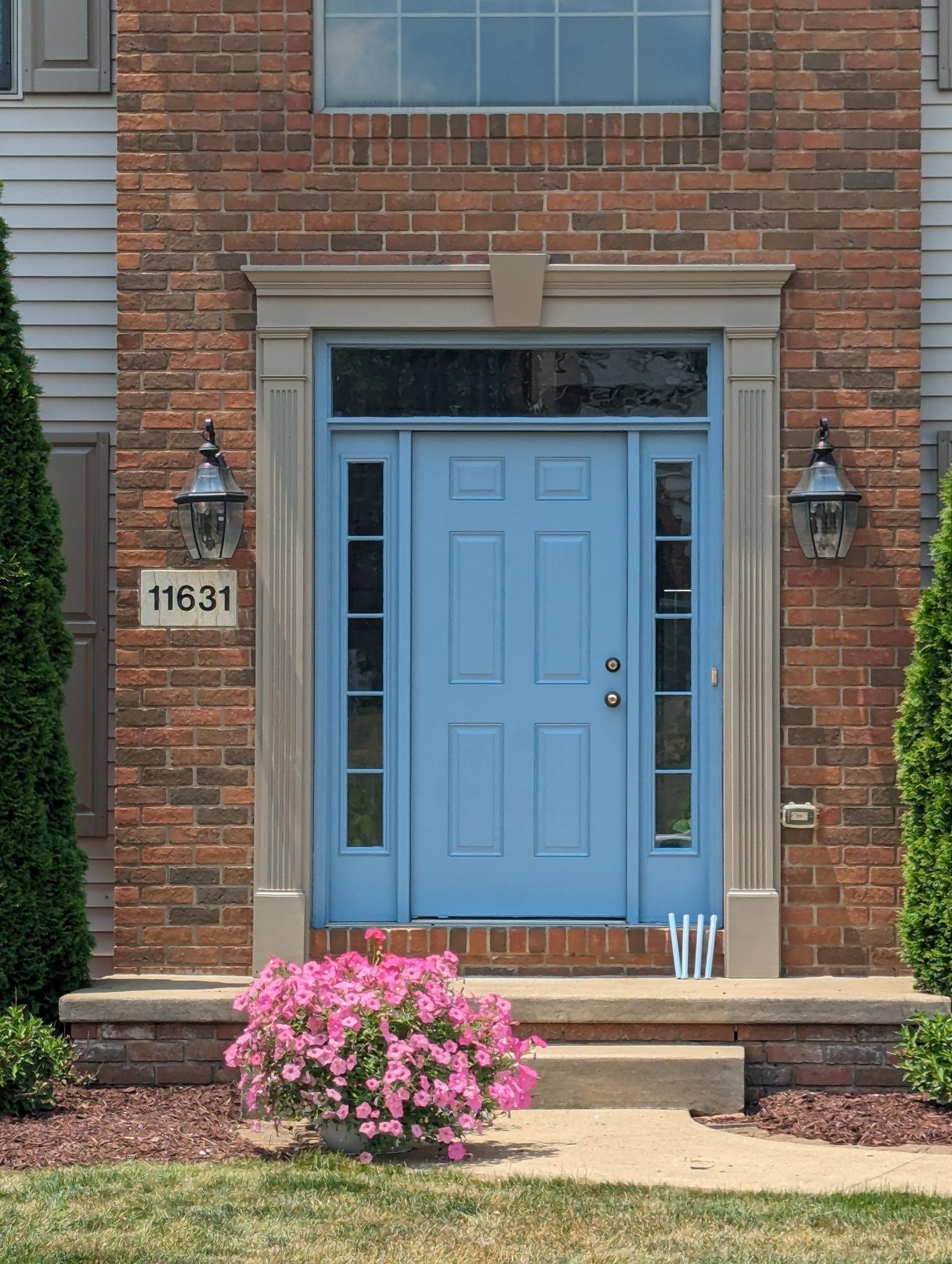 Brick townhouse entrance with light blue door, house number 11631, and pink flowers by the steps