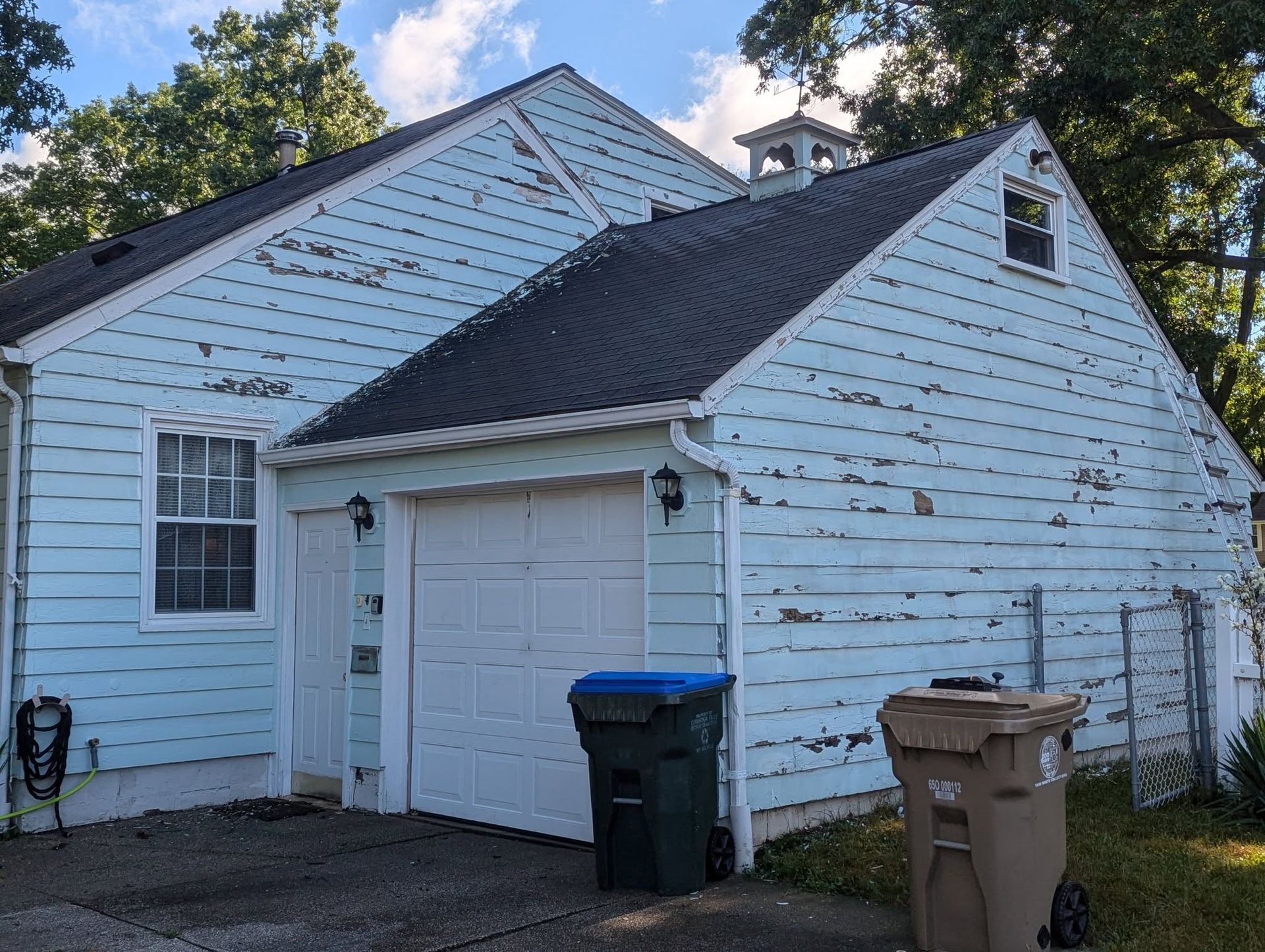 Blue house with white trim and detached garage, with trash bins in the driveway