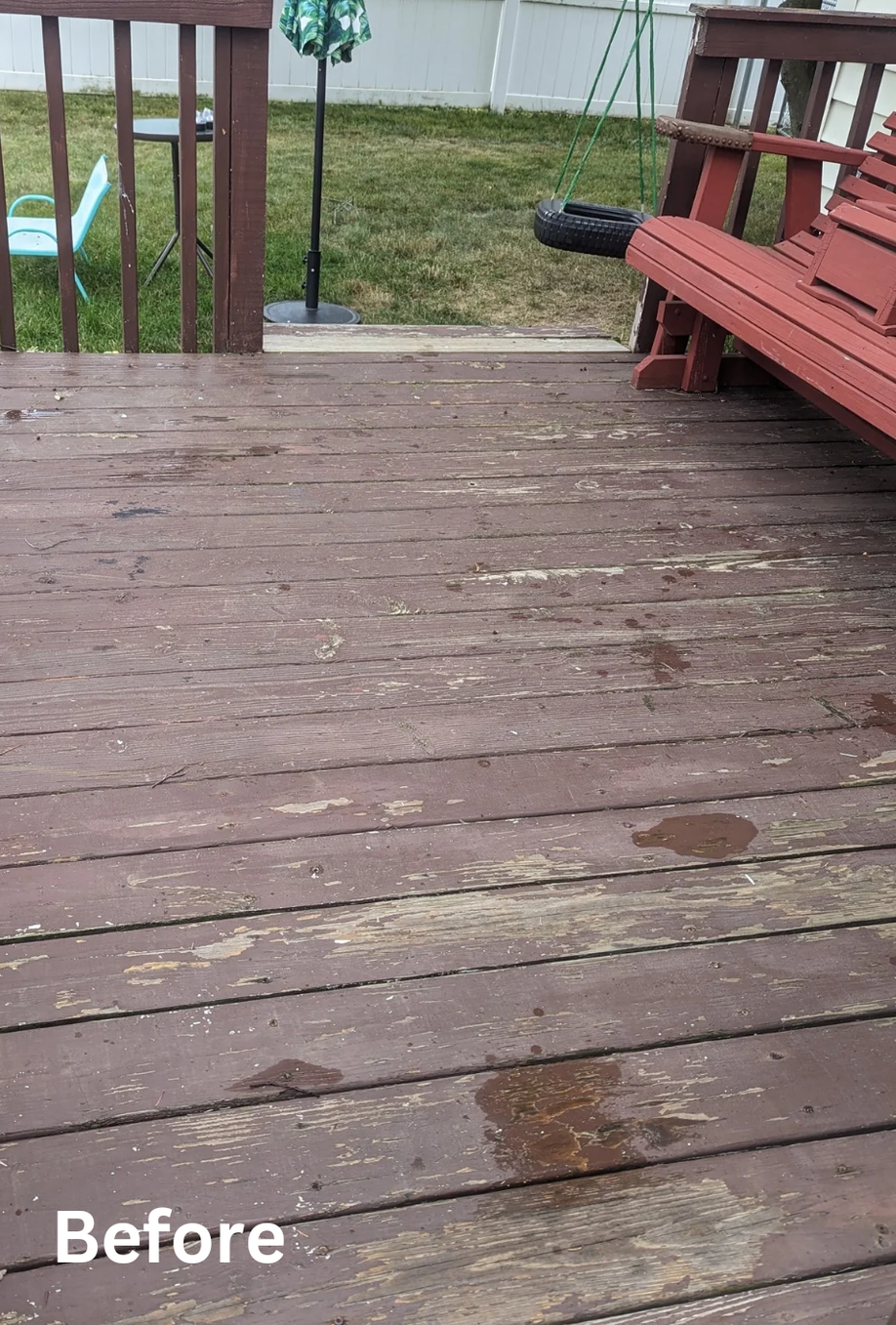 Weathered wooden deck with peeling paint, red bench, and grassy yard beyond railing.