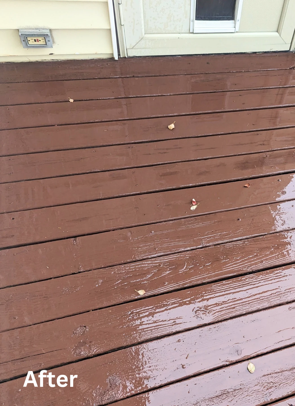 Brown wooden deck after cleaning, with a few wet streaks and small leaves near a white door.