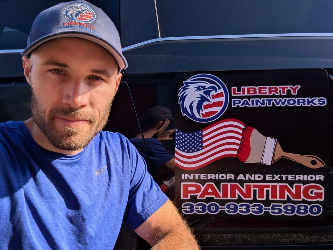 Man in blue shirt and cap beside Liberty Paintworks truck with logo and “Interior and Exterior Painting” text