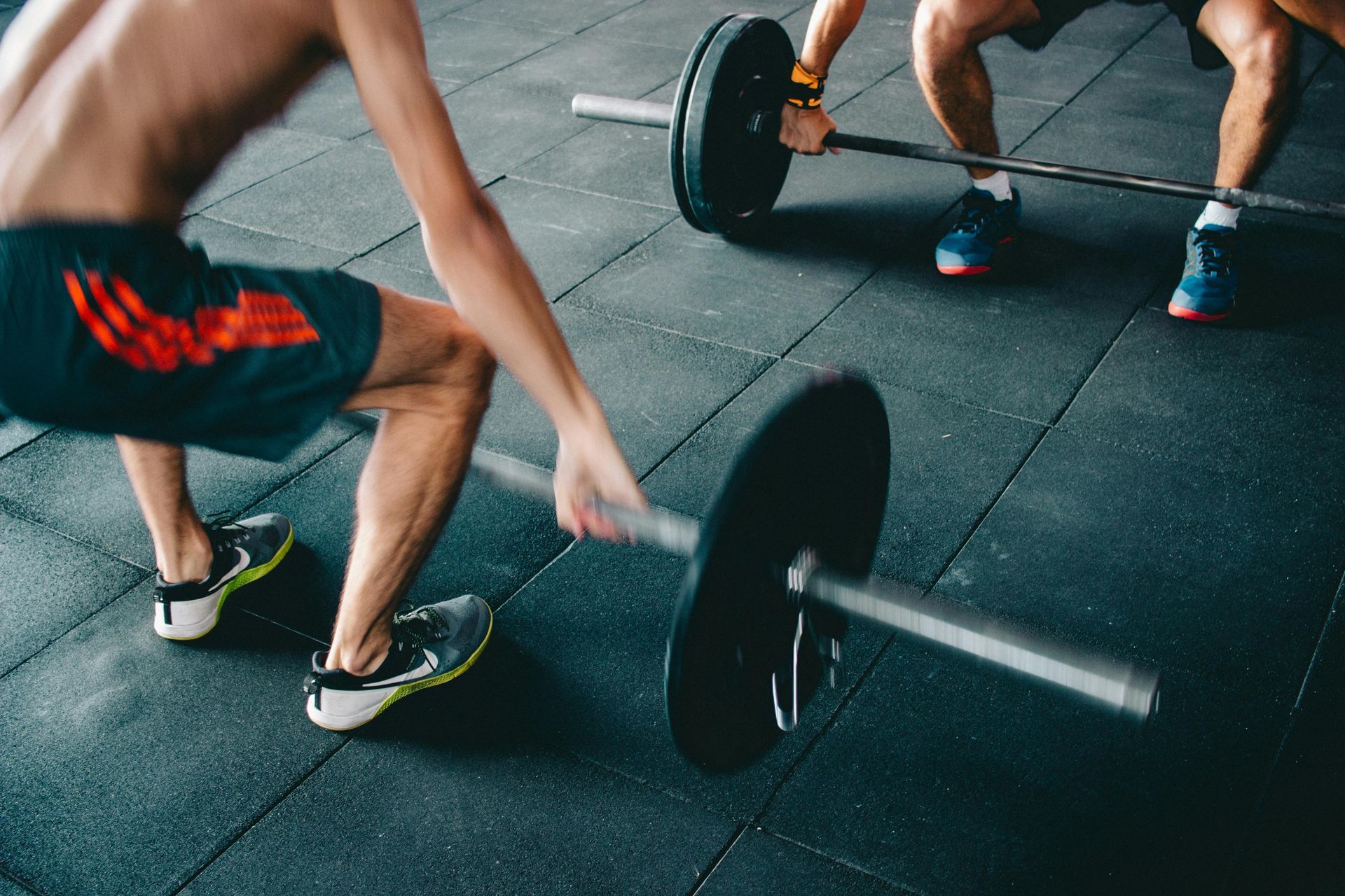 People exercising with barbells on a gym floor, mid-lift