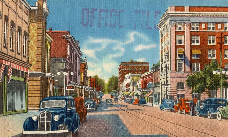 Street scene with vintage cars and buildings. The sky has the faded text
