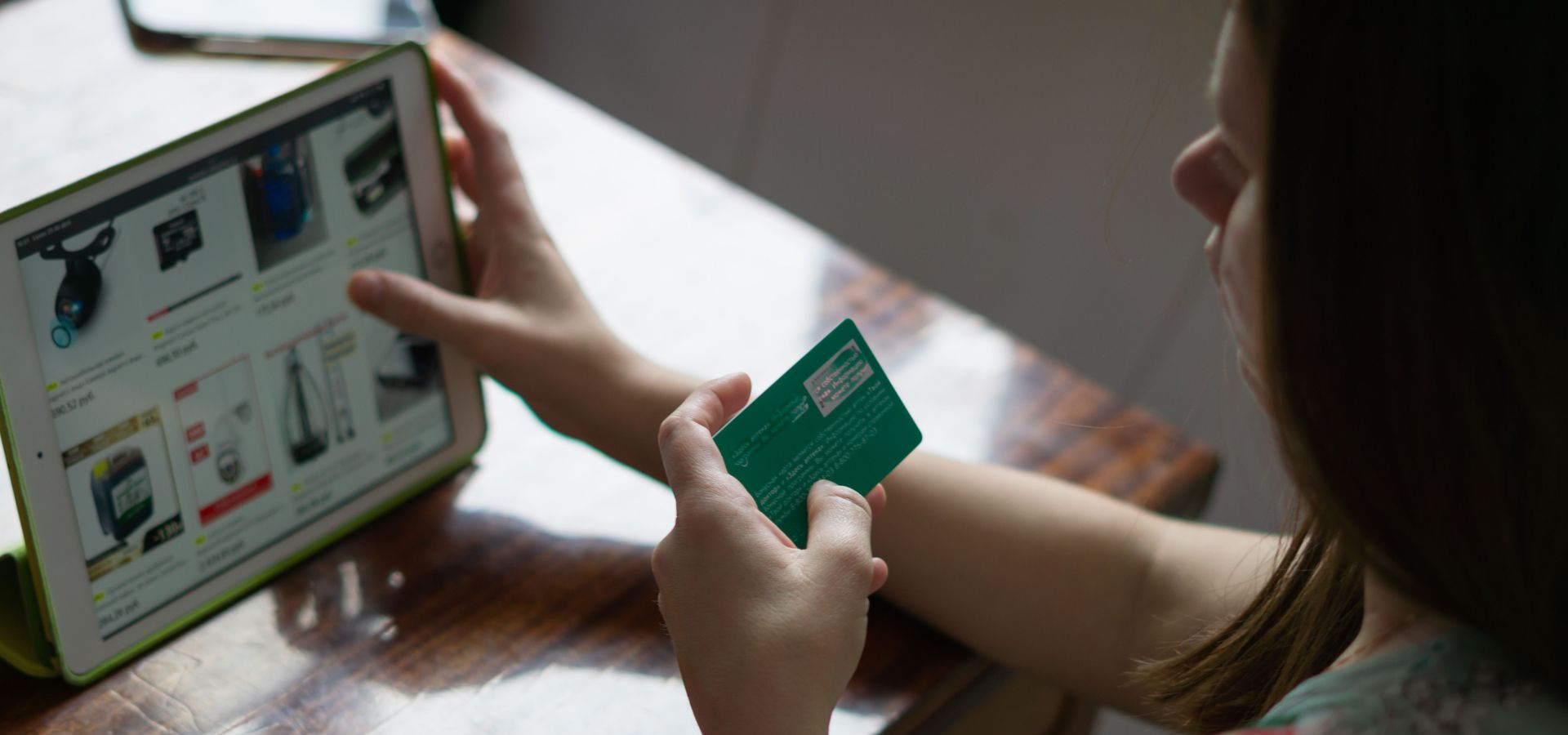 Person holding a green credit card while shopping on a laptop screen