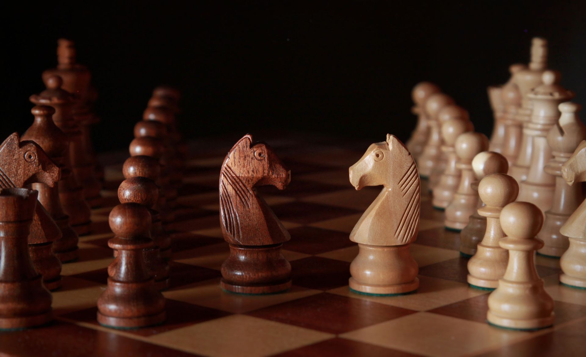 Wooden chess pieces arranged on a chessboard, with dark pieces on the left and light pieces on the right.