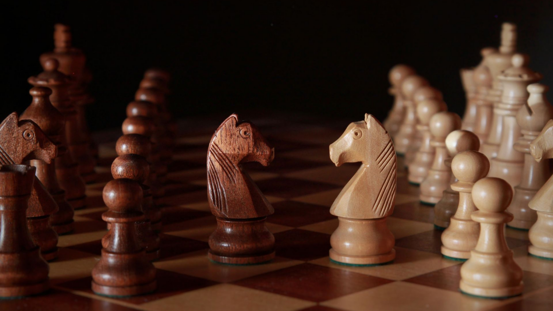 Chess pieces arranged on a board, with white and brown pieces facing each other in warm light.
