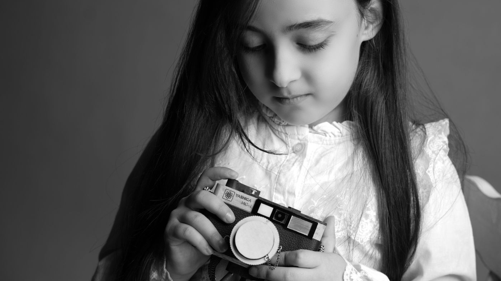 Young girl holding a camera and looking down at it in black and white.