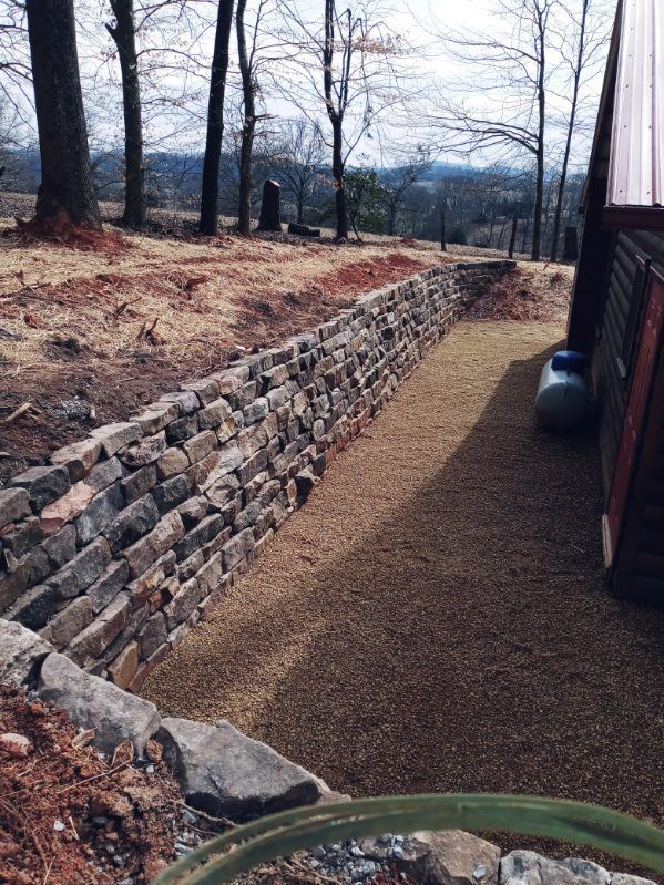 A stone wall is being built in a yard with trees in the background.