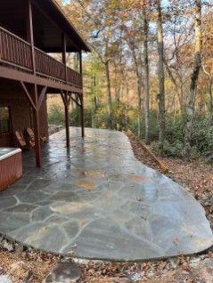 A large patio with a hot tub in front of a house in the woods.