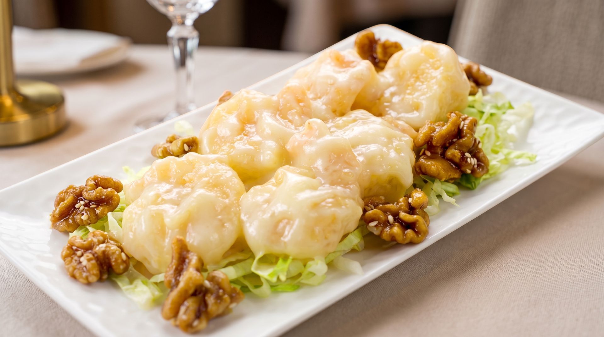 Shrimp in creamy white sauce garnished with walnuts on a rectangular white plate