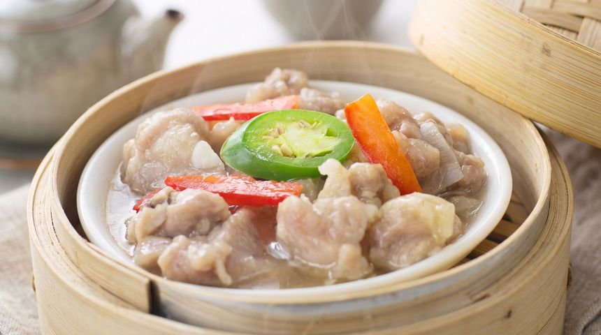 Steaming dumplings in a bamboo steamer, topped with sliced green chili and red pepper strips
