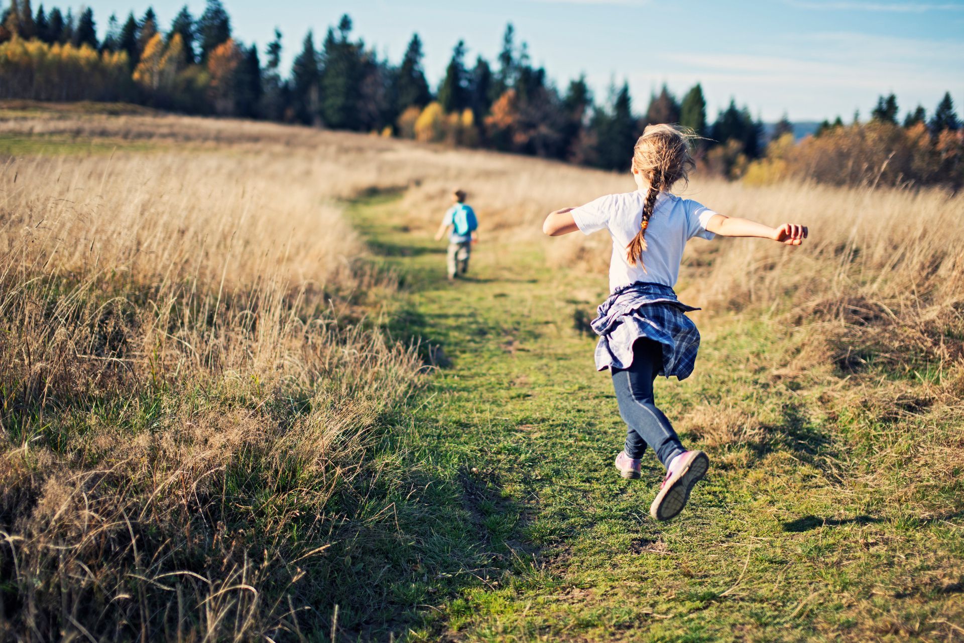 Boy and girl running along a path toward a forest