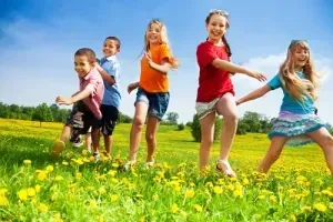 A group of children are running through a field of yellow flowers.