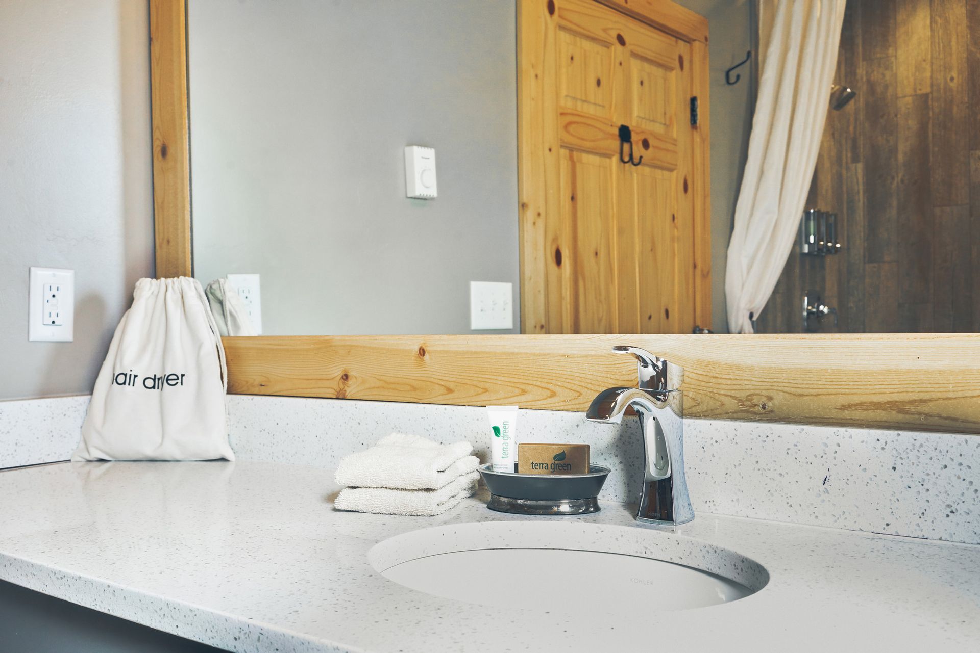 Bathroom sink with granite countertop, mirror, soap dispenser, and wooden door reflected behind it