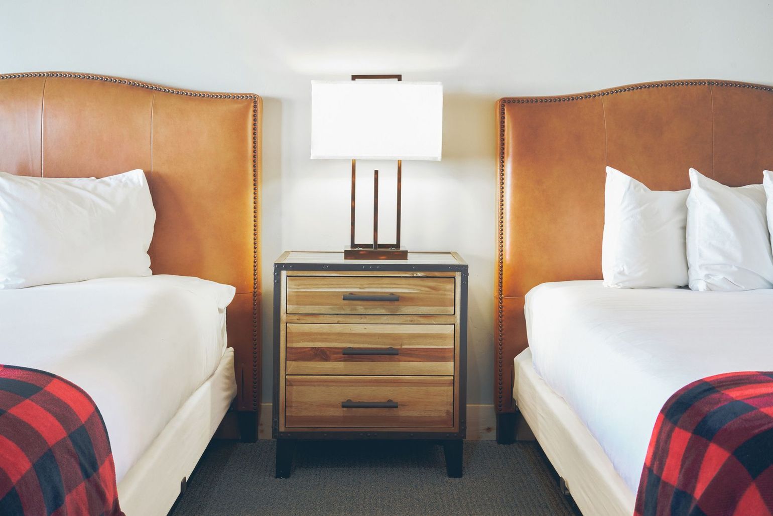 Twin hotel beds with white linens, wood nightstand, and a lamp between them