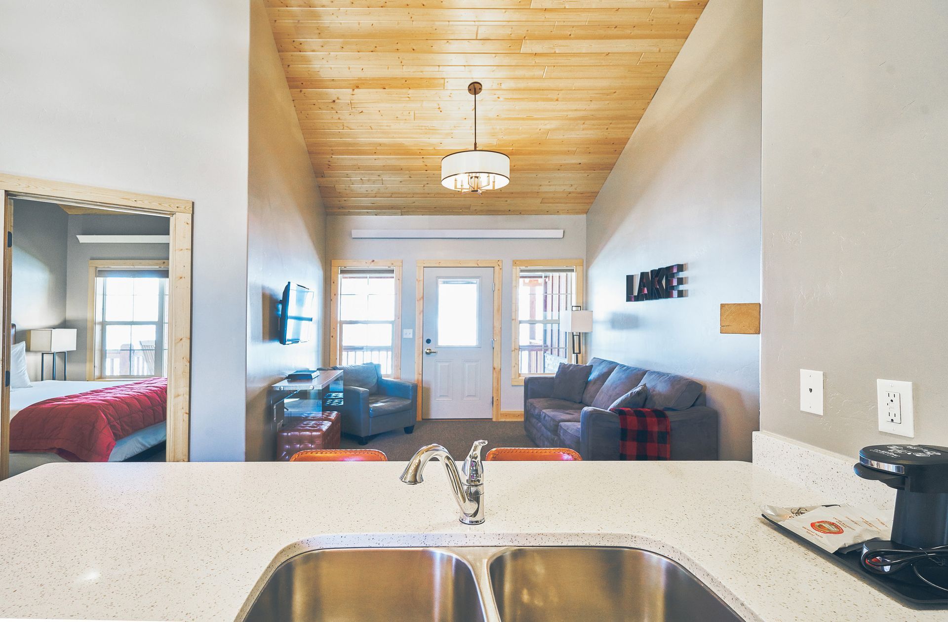 Bright kitchen sink overlooking a cozy living room with couch, TV, and glass doors.