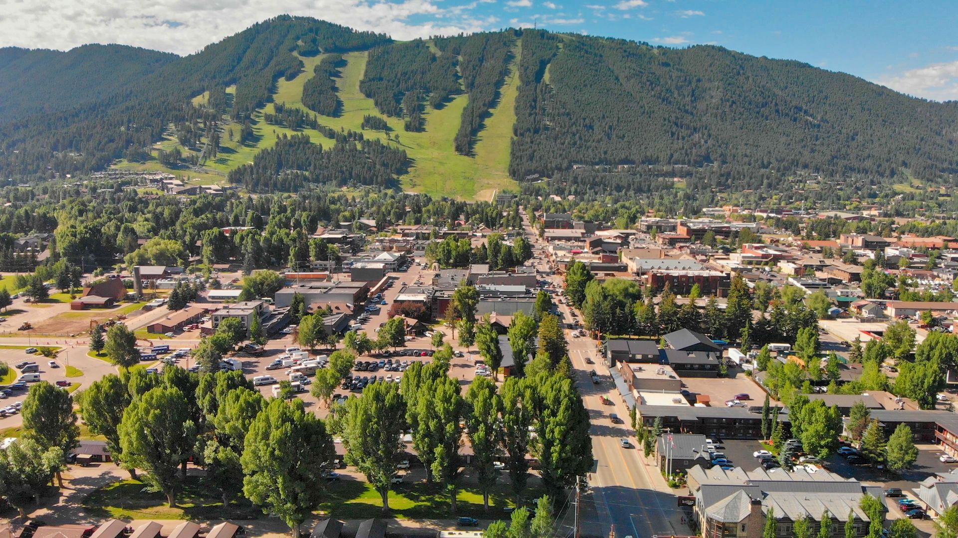 Aerial view of a town beside a mountain with ski trails and green trees in the foreground