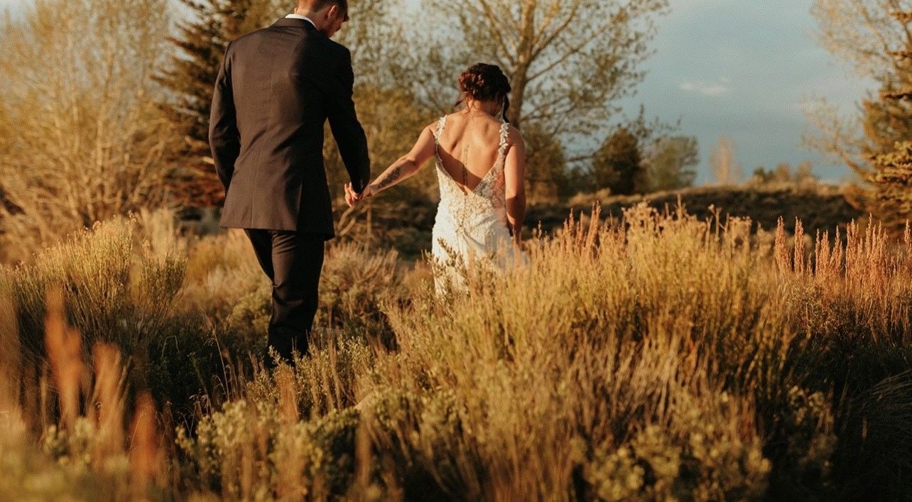Couple walking hand in hand through tall golden grass at sunset