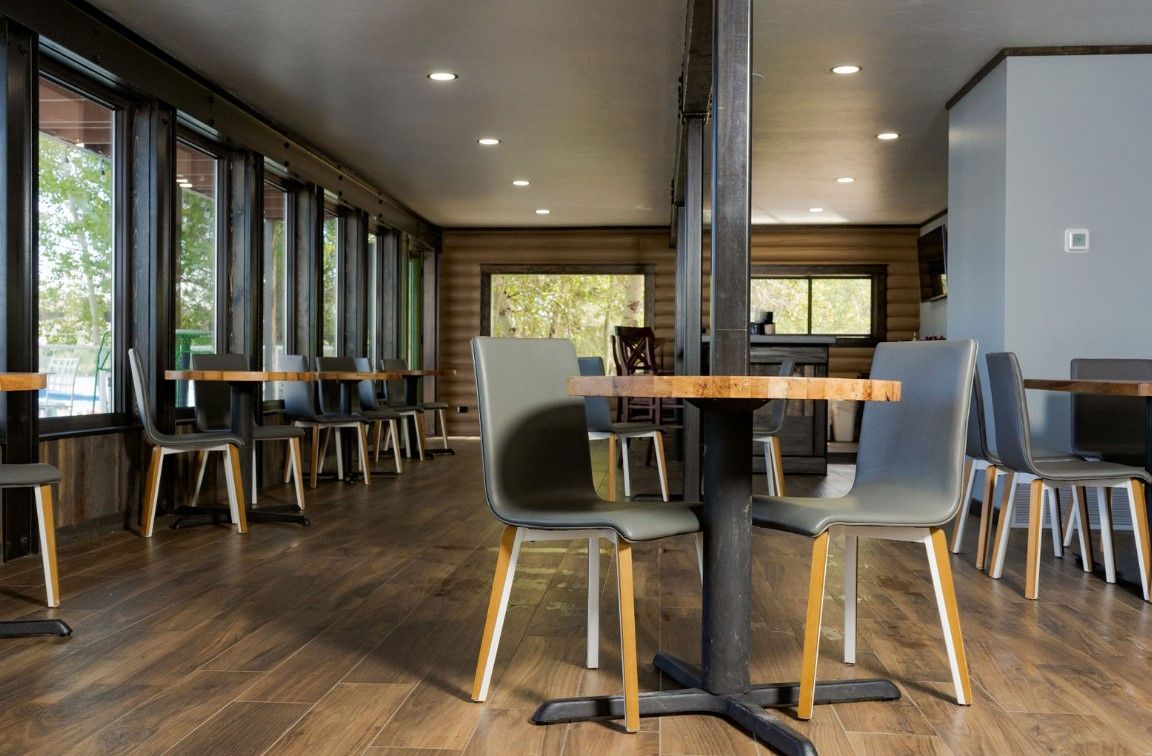 Empty modern café with wooden tables, gray chairs, and large windows letting in natural light