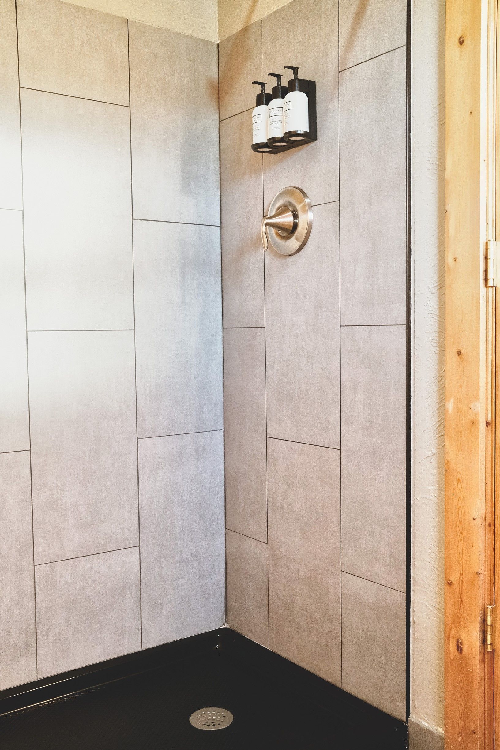 Tiled shower corner with a brass control and black shower floor drain