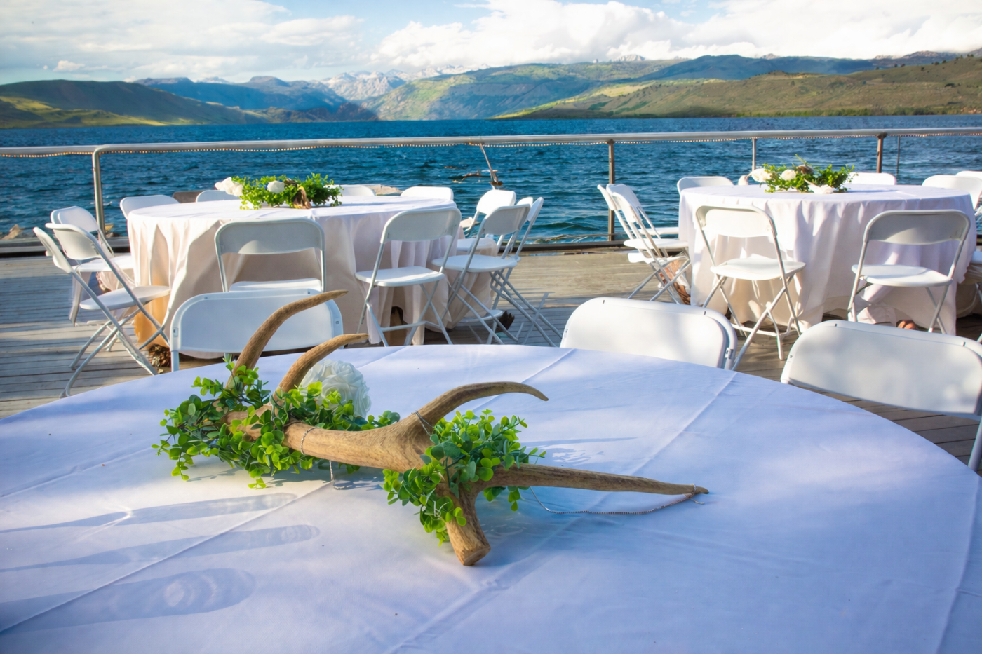 Outdoor banquet tables with white linens by a lake, mountains in the background