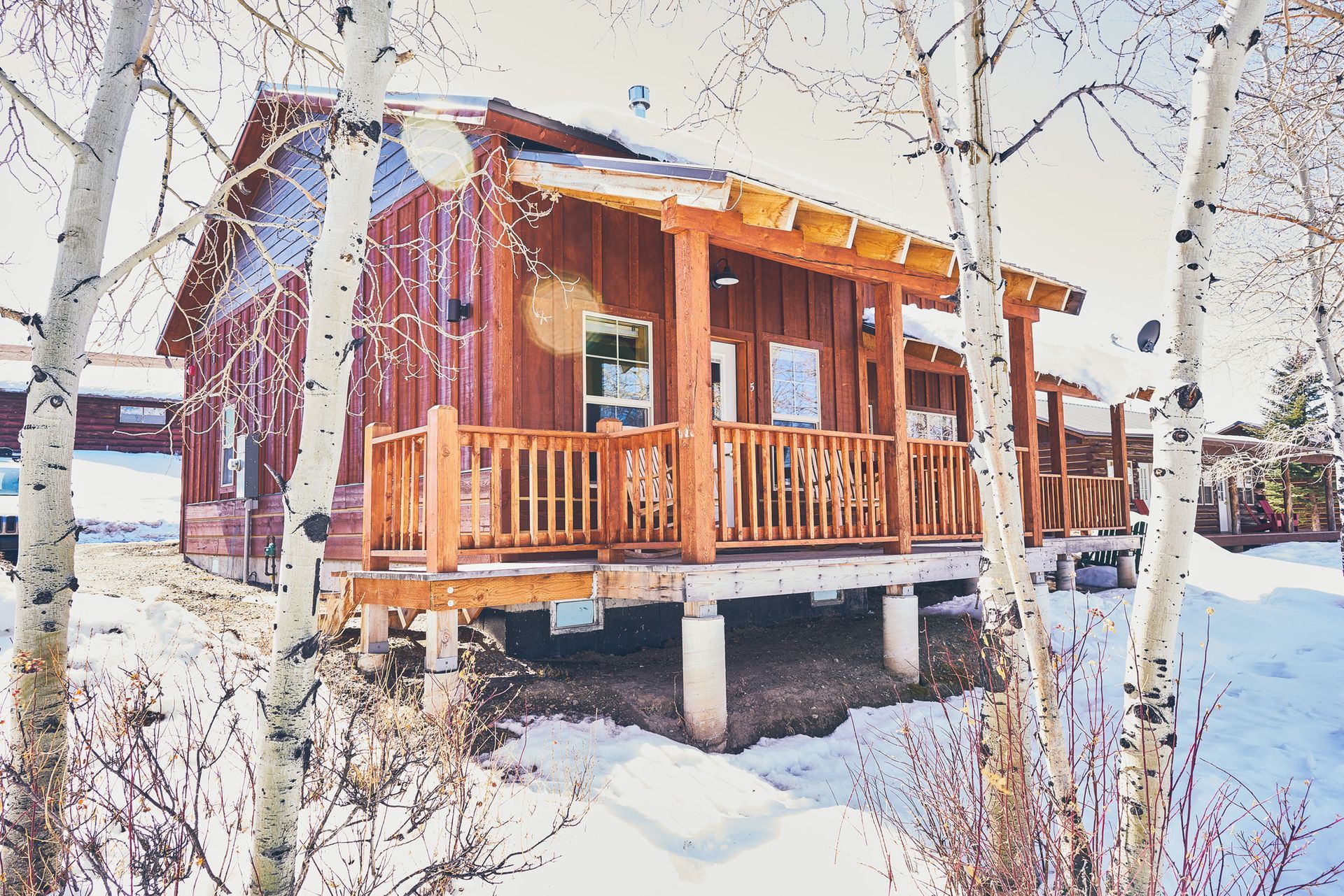 Snowy wooden cabin with a porch and bare trees in winter