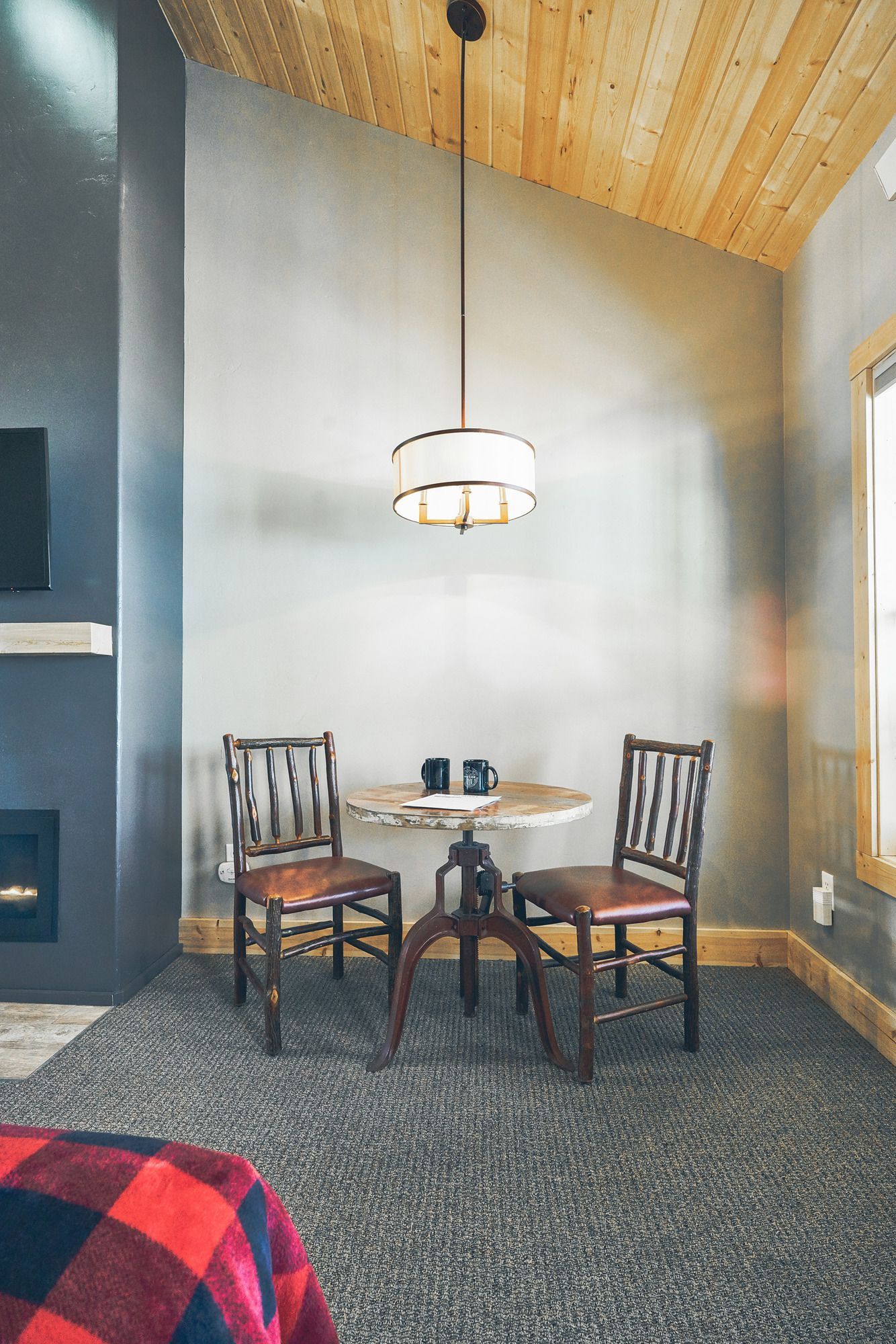 Small dining nook with two wooden chairs, round table, pendant light, gray walls, and wood ceiling.