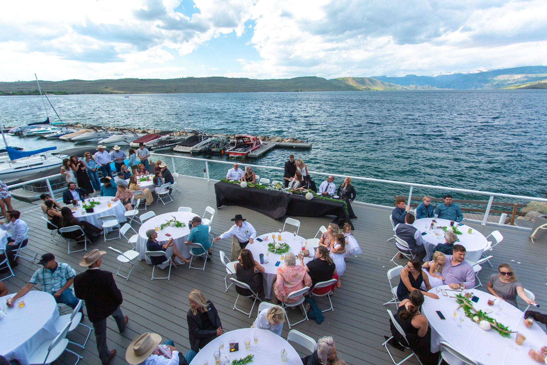 People dining on a boat deck overlooking choppy water and distant mountains under a bright sky