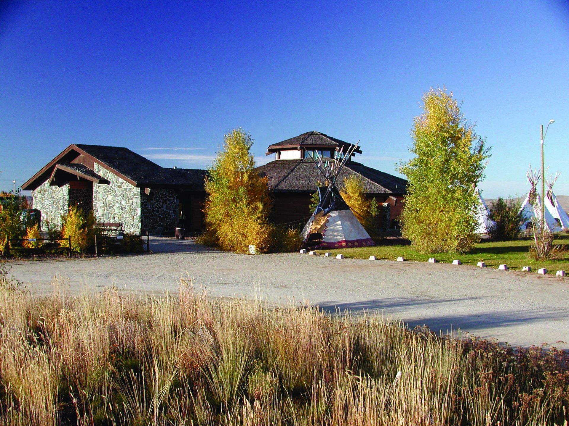 Rustic lodge with autumn trees beside a gravel lot under a clear blue sky.