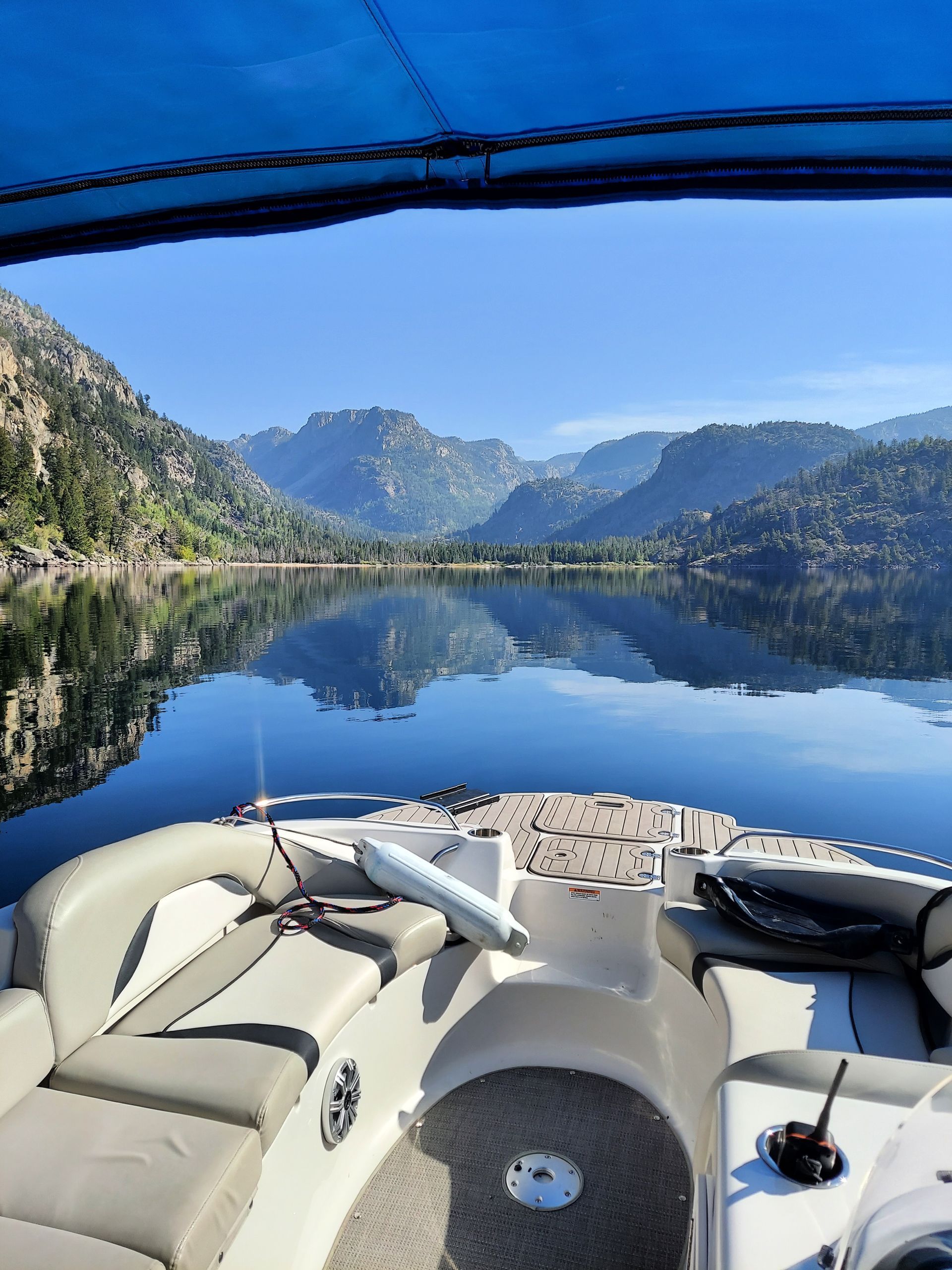 Boat lounge on a calm mountain lake, with blue sky and mirrored peaks in the water.