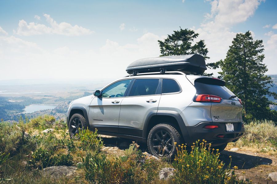 Silver SUV parked on a mountain overlook with trees and a cloudy valley view