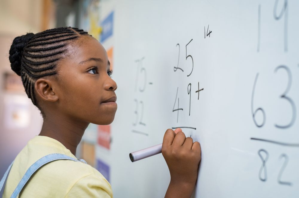Black girl student at blackboard doing mathematical calculations.
