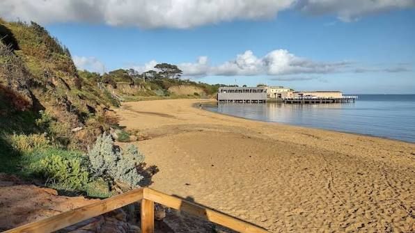 Sunny sandy beach with rocky cliffs and a pier over calm blue water
